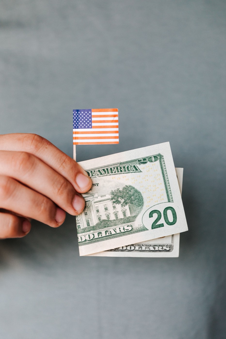 Hand holding U.S. dollar bills next to a small American flag
