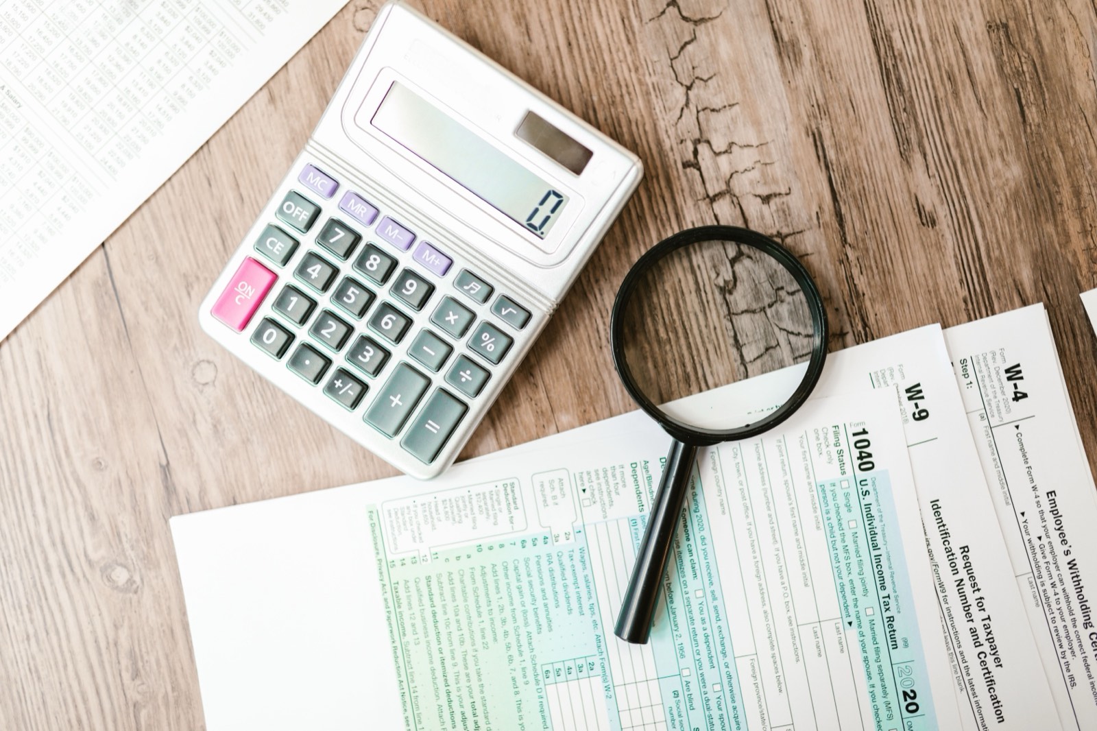 Tax forms, a calculator and a magnifying glass on a wooden desk