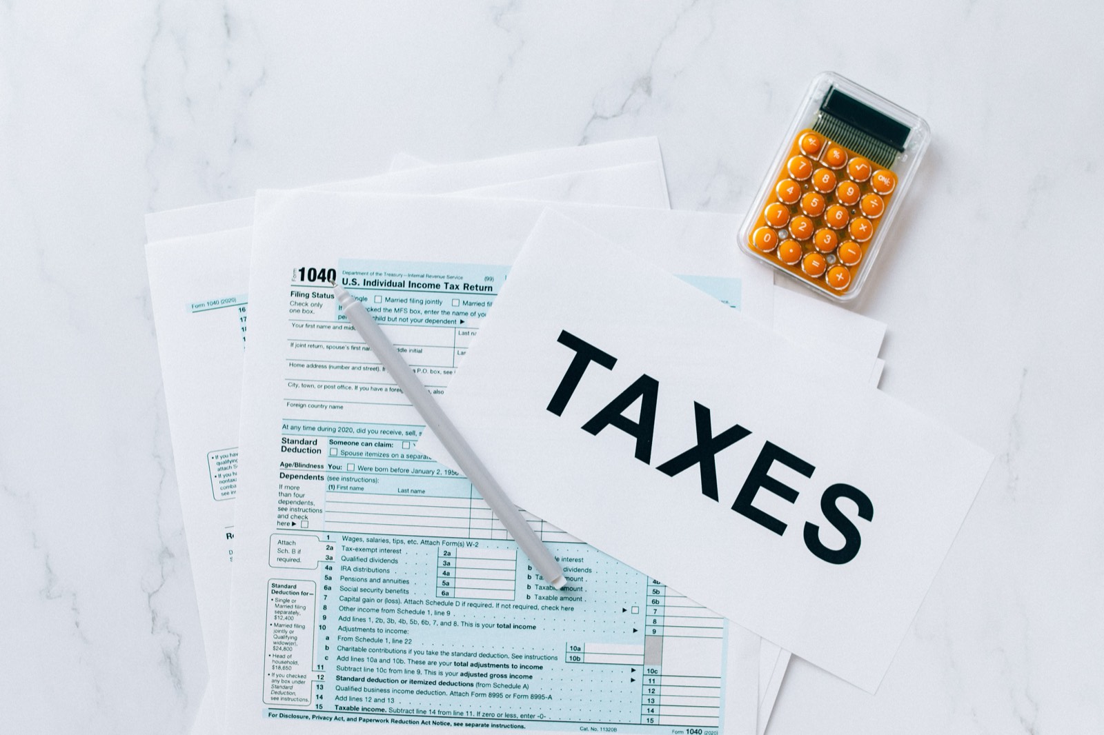 Tax forms on a desk with a sign that reads TAXES, a pen and a calculator